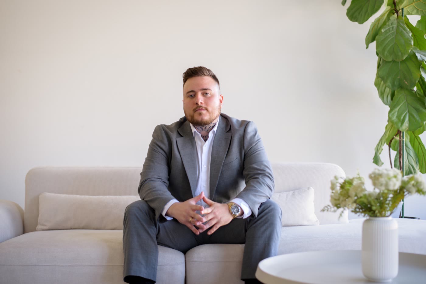 Maxime Patry, assis sur un divan blanc en veston gris, les mains jointes, dans un bureau lumineux